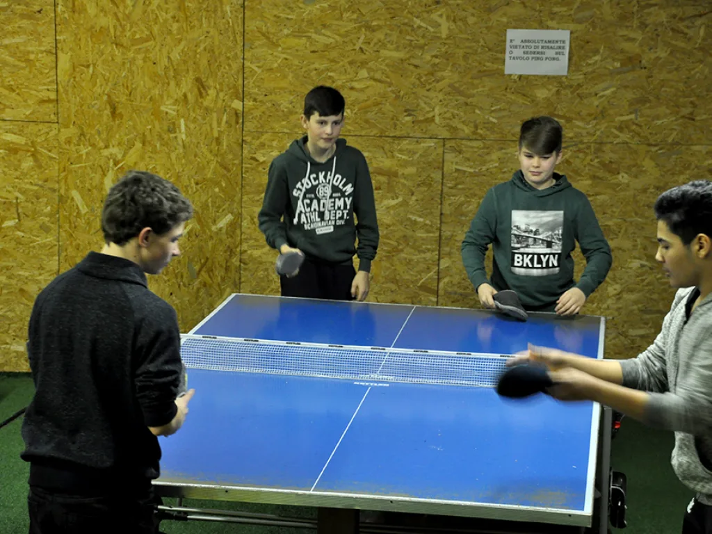 Zwei Jugendliche spielen Tischtennis, andere schauen zu.